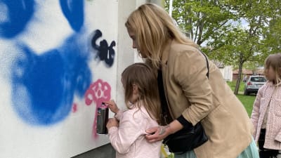 En mamma och en liten flicka sprejar grafitti på skolbyggnad.