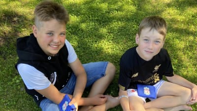 Två unga killar sitter i gräset med varsin plånbok i famnen.