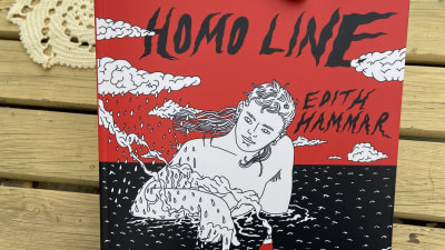 Två händer håller i boken "Homo Line", ovanför ett bord med en liten duk. 