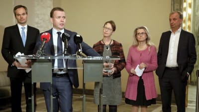 Petteri Orpo står och håller tal. I bakgrunden syns Kai Mykkänen, Sari Essayah, Päivi Räsänen och Harry Harkimo.