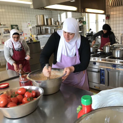 Tre kvinnor med huvudduk lagar mat i ett storkök.