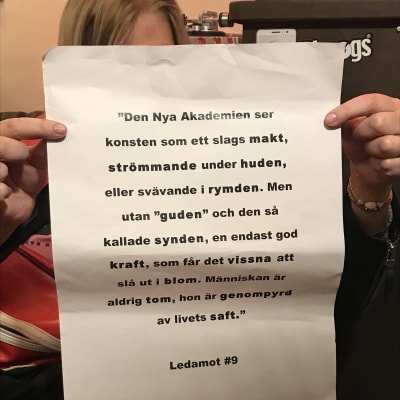 En person håller upp ett papper med texten "Den nya Akademien ser konsten som ett slags makt..."