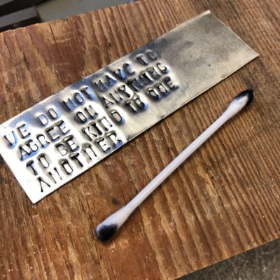 Aluminumplatta med svärtad text och en bomullspinne på en träplatta