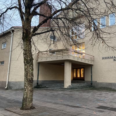 Vaalean rakennuksen seinässä lukee Hermannin koulu. Koulun edessä on lehdetön puu. 
