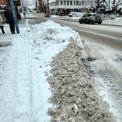 Auto ajaa kadulla, jonka sivussa lumikinoksia.