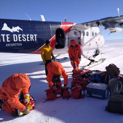 Henkilöt tutkivat laukkuja lentokoneen vieressä Etelämantereella.