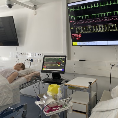 Kaksi nukkea potilassängyissä makaamassa, seinällä monitoreja. Hoitotyön luokka.