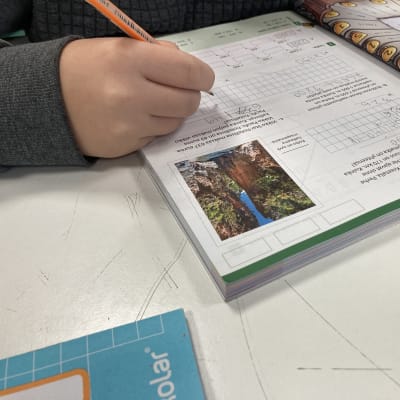 Koululainen tekee matematiikan tehtäviä kynä kädessään.