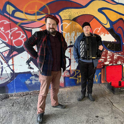Kaksi miestä seisoo graffitien edessä. 