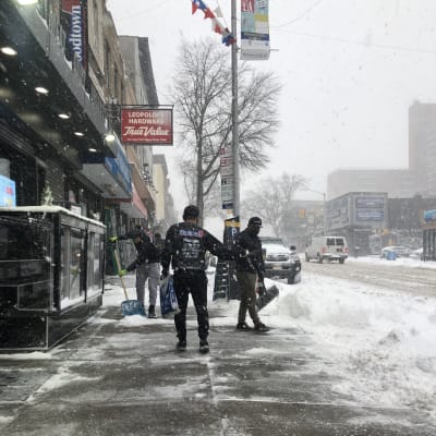 Folk skyfflar bort snö på en gata i New York.