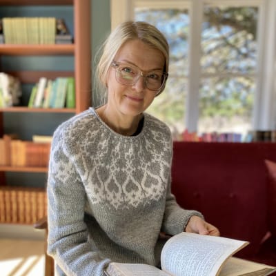 Anna Påfs-Streng sitter i Strömsös biliotek med en uppslagen bok i famnen.