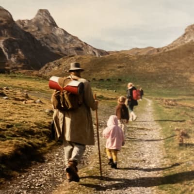 Perhe kävelee jonossa vuoristomaisemassa. He ovat selin kameraan ja viimeisenä kulkee perheen isä Otso Kautto.