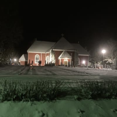 Valaistu kirkkorakennus erottuu muuten pimeässä lumimaisemassa.