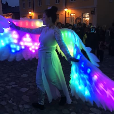 En kvinna utklädd till en ängel med stora vingar som lyser i olika färger.