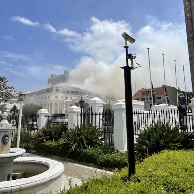 Rök ovanom parlamentsbyggnaden i Kapstaden. Den är omgiven av stängsel.