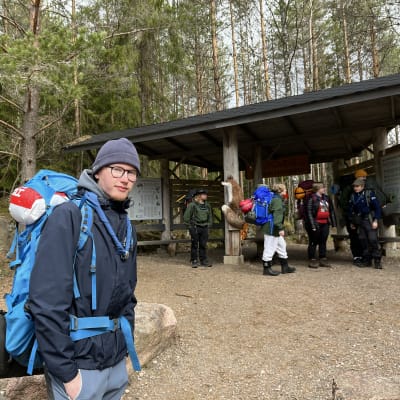 Partiolainen seisomassa rinkka selässä. Taustalla muita hänen partiokavereitaan.