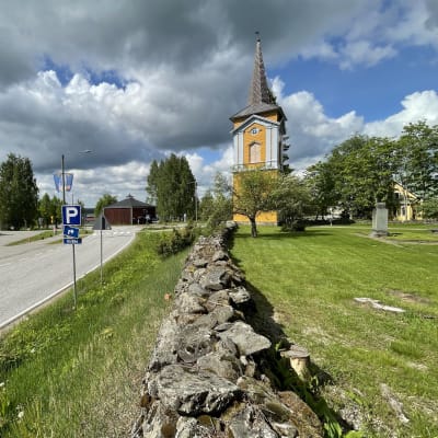 Kiihtelysvaaran keltainen kellotapuli ja etualalla kirkon vanhaa kiviaitaa.