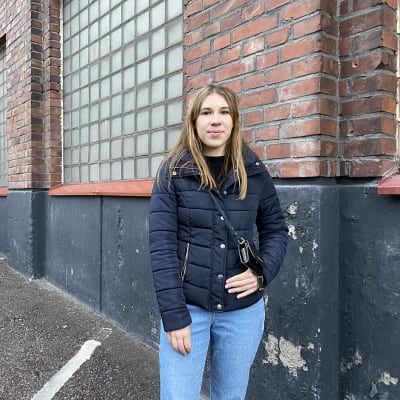 Julia Rumyantseva seisoo tiilisen rakennuksen edessä ja hymyilee kameralle.