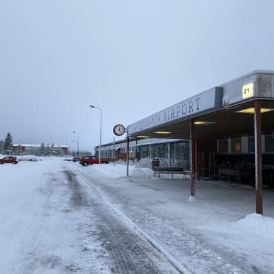 Etualalla on Lappeenrannan lentoasemarakennus ja taustalla näkyy joitakin autoja parkkipaikalla. Sää on pilvinen, maassa on lunta.