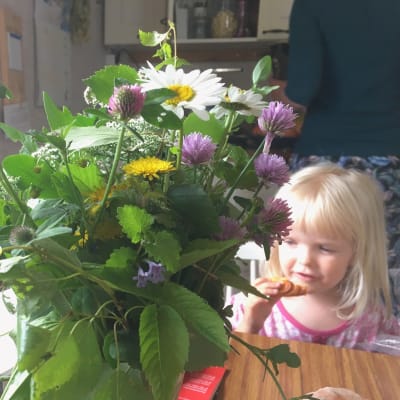 Ines Holmström äter bulle bakom en bukett med ätbara växter.