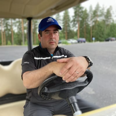 Mikko Saarela istuu golfautossa, kädet ratin päällä. 