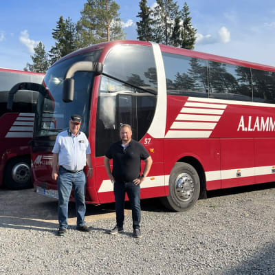 Kaksi miestä seisoo kahden punavalkoisen bussin edessä.