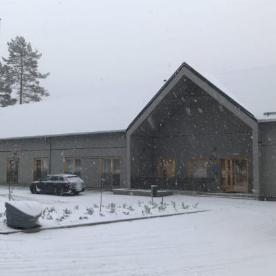 Iso yksikerroksinen rakennus metsän laidassa.