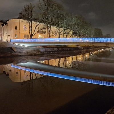 Biblioteksbron i Åbo lyser i blått och speglas i Aura å en sen natt.