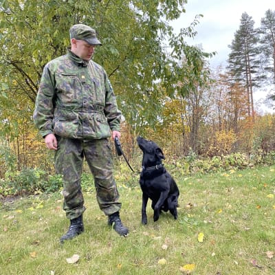 Vääpeli Mika Pitkänen seisoo huumekoiransa Speedyn kanssa syksyisessä maisemassa.