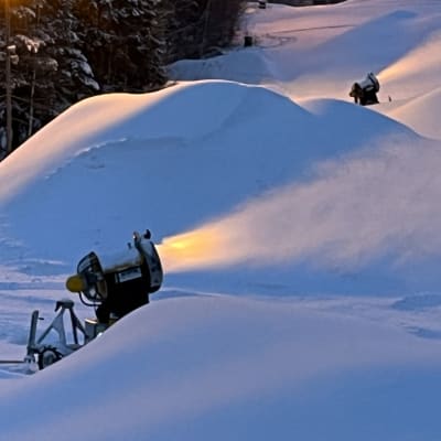 Kaksi lumitykkiä lumettaa laskettelurinnettä.