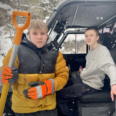 Leevi Heikkinen oranssi-mustassa talvitakissa koppimönkijän edessä lapio kädessä, taustalla Viljam Erkkilä koppimönkijän ratissa.
