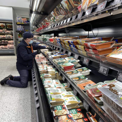 Oriveden K-Supermarketissa lihamestari Jari Pohjonen järjestelee polvillaan hyllyn edessä seisoen eineksiä hyllylle