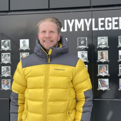 Roope Korhonen seisoo Sotkamon pesäpallostadionilla Jymylegandat -taulun edessä.