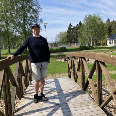 Mies nojaa kapean, puisen kävelysillan kaiteeseen. 
