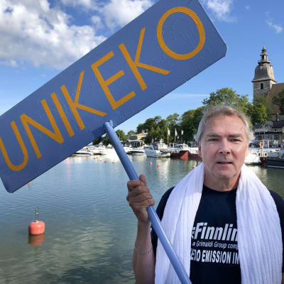 Tom Pippingsköld pitelee Unikeko-kylttiä Naantalin vanhan kaupungin rannassa.