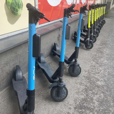 Pitkä rivi sähköpotkulautoja pysäköitynä marketin eteen.