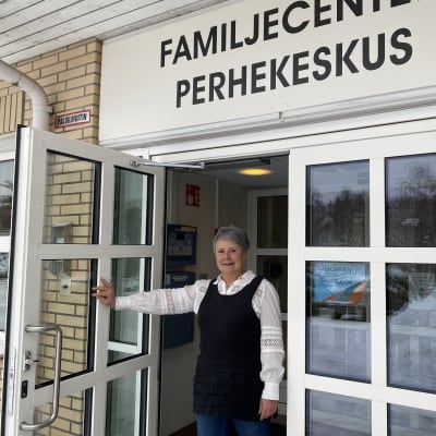 En kvinna som står och håller upp en glasdörr.