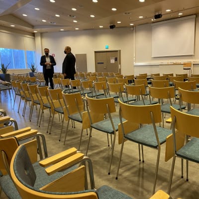 Kaksi miestä isossa salissa, paljon tyhjiä tuoleja. Tähtisali Tampereen Messu- ja urheilukeskuksessa. 