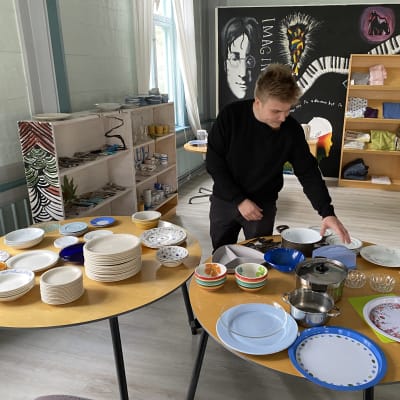 Olavi Huvi järjestelee lahjoituksena saatuja astioita Ohjamon pöydälle. 