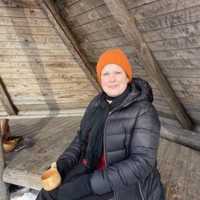 Talvivaatteisiin pukeutunut nainen istuu laavulla kuksa kädessä. Luontolähetti Annika Peurasaari Kemistä.