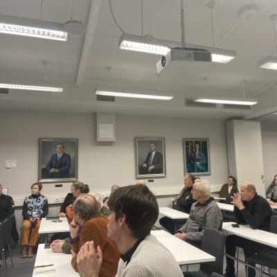 Ihmisiä Kuhmon kaupungintalon valtuustosalissa keskustelutilaisuudessa.