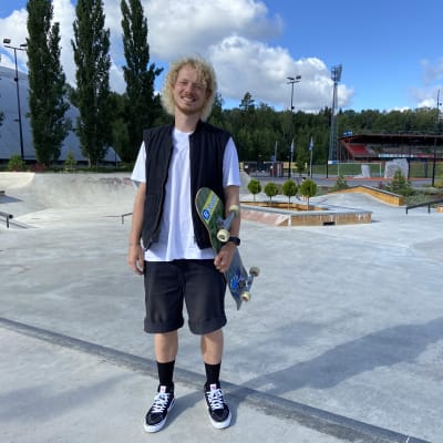 Taneli Eriksson står framför Myrbacka skatepark. Han håller sin skateboard i handen och ler in i kameran.