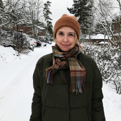 En kvinna med ljust hår står i ett vinterlandskap och ler in i kameran