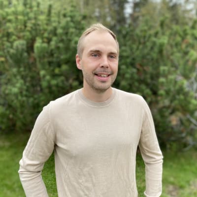 Man i beige tröja står i en trädgård.