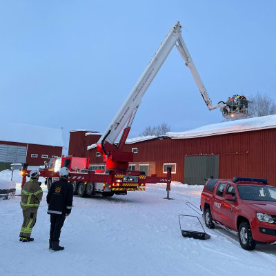 Pelastuslaitoksen työntekijät nostavat nosturin avulla pelastajia navetan katolle.