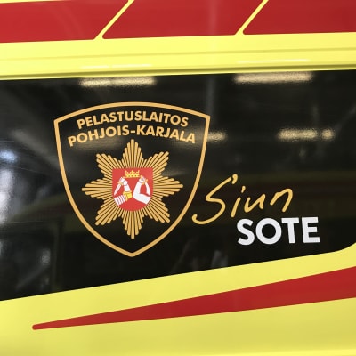 Pohjois-Karjalan pelastuslaitoksen logo ambulanssin kyljessä.