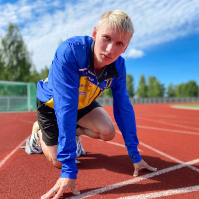 Vaaleahiuksinen, siniseen juoksutakkiin pukeutunut Samuli Samuelsson valmiina lähtemään juoksuun Ikaalisten kentällä. Taustalla näkyy urheilukenttää ja sinistä taivasta.
