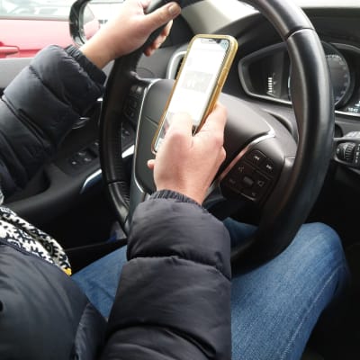 Person läser något på telefonen samtidigt som hen kör bil.