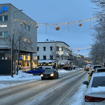 katunäkymä Lohjalta, jouluvalot roikkuvat vielä kadun yläpuolella, lunta tiellä ja aurattuna reunassa, autoja pysäköitynä kadunvarteen, osa autoista ajaa kadulla.