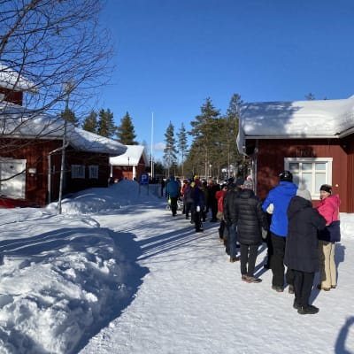 Äänestäjiä jonossa punaisen talon edessä.